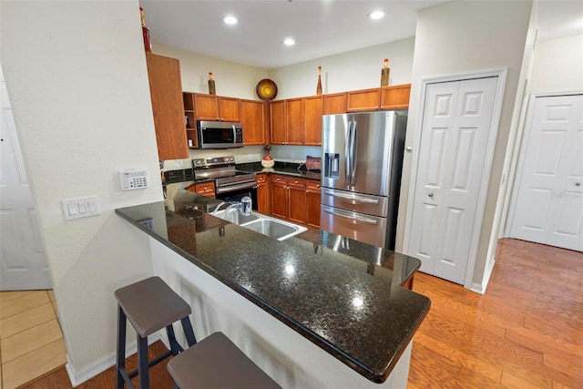 kitchen with kitchen peninsula, appliances with stainless steel finishes, a kitchen breakfast bar, sink, and dark stone countertops