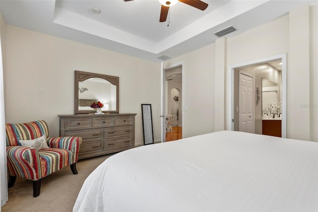 carpeted bedroom featuring a tray ceiling, ensuite bath, and ceiling fan