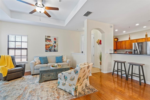 living room featuring a raised ceiling, ceiling fan, and light hardwood / wood-style flooring