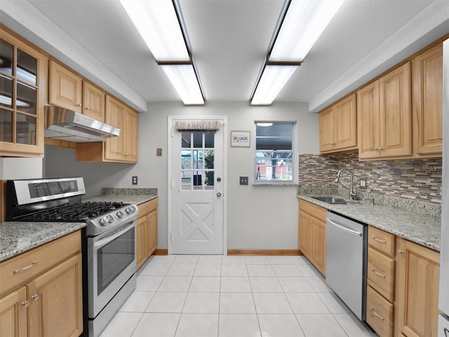 kitchen with backsplash, light stone counters, stainless steel appliances, sink, and light tile patterned flooring