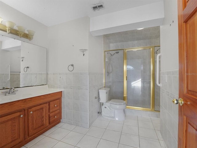 bathroom featuring tile patterned flooring, toilet, vanity, a shower with shower door, and tile walls