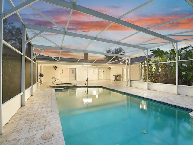 pool at dusk featuring an in ground hot tub, glass enclosure, and a patio area