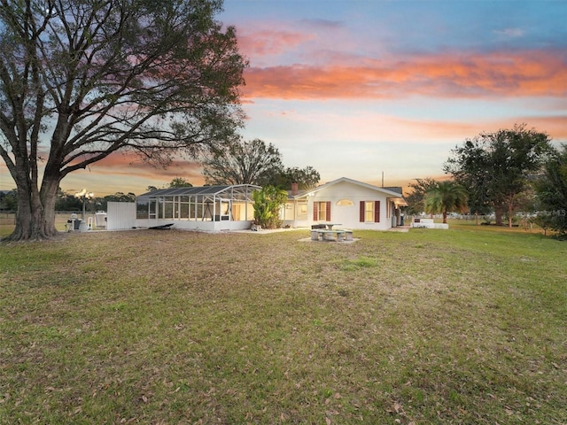 yard at dusk featuring glass enclosure and an outdoor fire pit