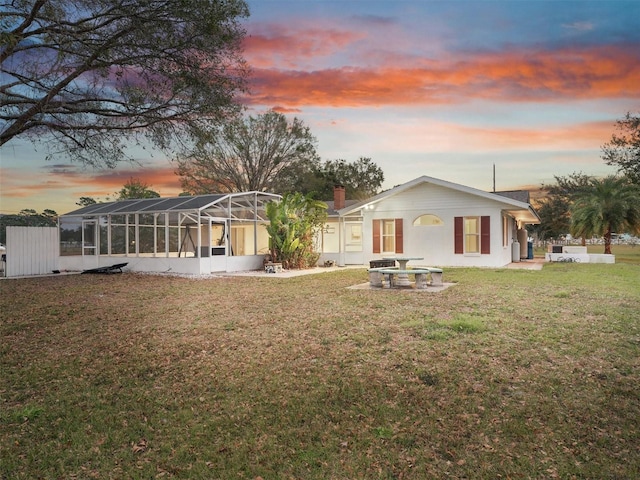 back house at dusk with a yard and glass enclosure