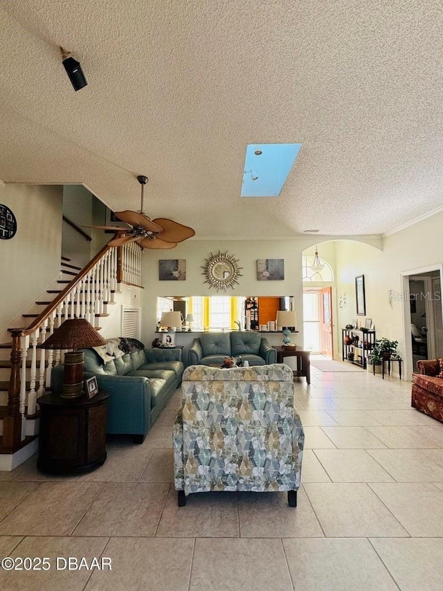 living room featuring light tile patterned floors, a textured ceiling, a skylight, and ceiling fan