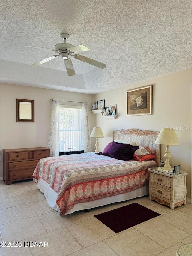 tiled bedroom with a tray ceiling, ceiling fan, and a textured ceiling