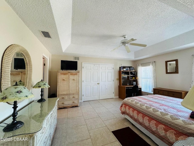 bedroom featuring a raised ceiling, ceiling fan, light tile patterned floors, a textured ceiling, and a closet