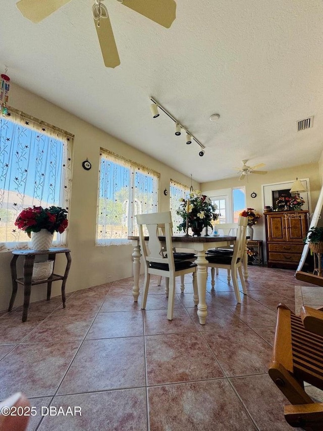 dining space featuring ceiling fan, tile patterned flooring, rail lighting, and a textured ceiling