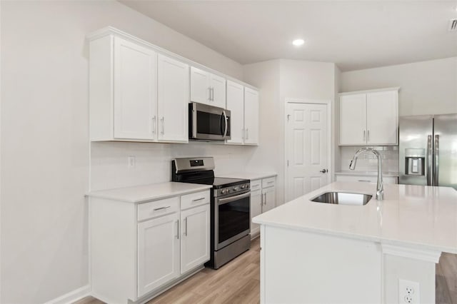 kitchen with a kitchen island with sink, sink, light wood-type flooring, white cabinetry, and stainless steel appliances