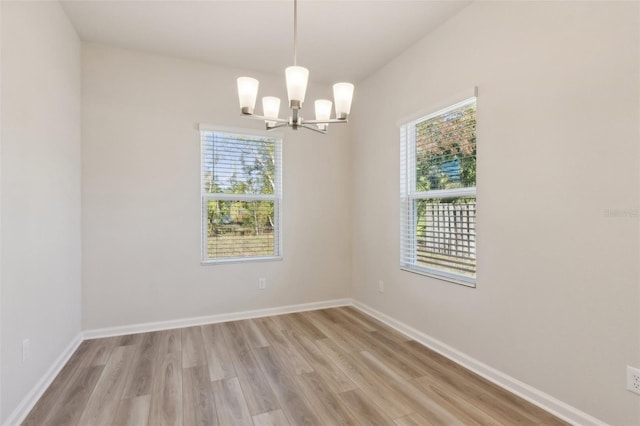 spare room with a healthy amount of sunlight, light wood-type flooring, and a notable chandelier