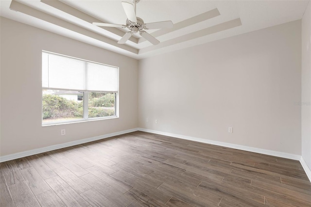 empty room featuring dark hardwood / wood-style flooring, a raised ceiling, and ceiling fan