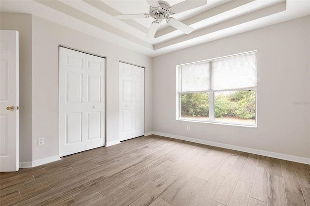 unfurnished bedroom with wood-type flooring, a raised ceiling, multiple closets, and ceiling fan