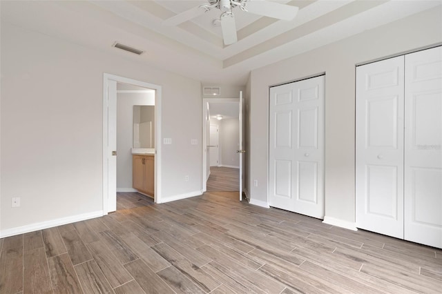 unfurnished bedroom featuring ensuite bath, a raised ceiling, two closets, and ceiling fan