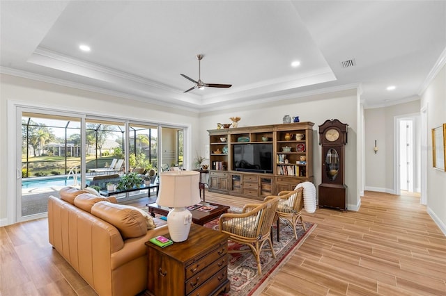 living room with a raised ceiling, ceiling fan, ornamental molding, and light hardwood / wood-style flooring