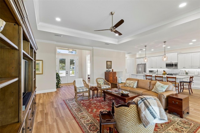 living room with a raised ceiling, ceiling fan, french doors, and light hardwood / wood-style flooring