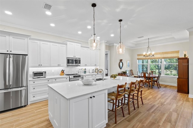 kitchen with hanging light fixtures, stainless steel appliances, a kitchen island with sink, white cabinets, and sink