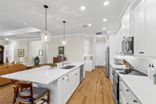 kitchen with stainless steel appliances, sink, white cabinets, a kitchen breakfast bar, and hanging light fixtures