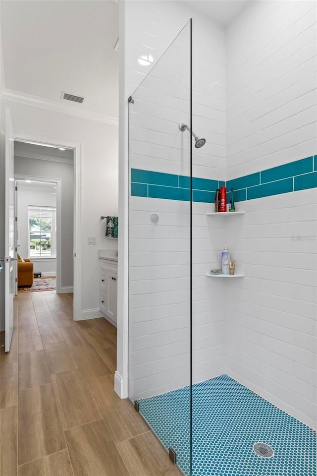 bathroom featuring ornamental molding, tiled shower, and wood-type flooring