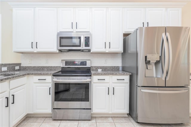 kitchen featuring dark stone countertops, appliances with stainless steel finishes, light tile patterned floors, white cabinets, and backsplash