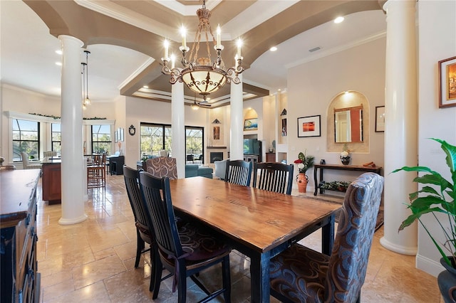 dining space with a high ceiling, ornate columns, a raised ceiling, ornamental molding, and a chandelier