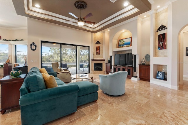 living room featuring ceiling fan, a raised ceiling, a towering ceiling, crown molding, and a high end fireplace