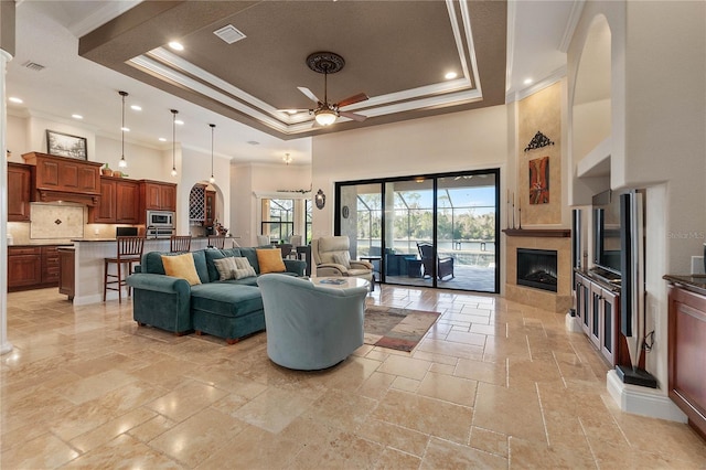 living room with ceiling fan, crown molding, a high ceiling, and a raised ceiling