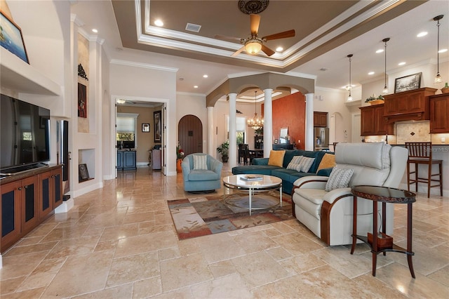 living room with a tray ceiling, ceiling fan with notable chandelier, ornamental molding, and ornate columns