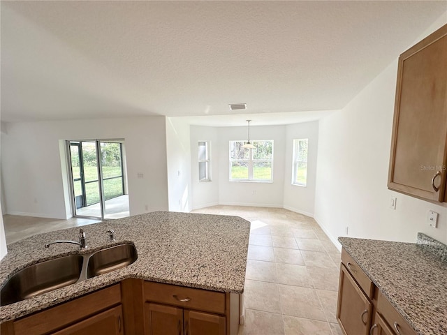 kitchen featuring decorative light fixtures, light stone countertops, light tile patterned flooring, and sink