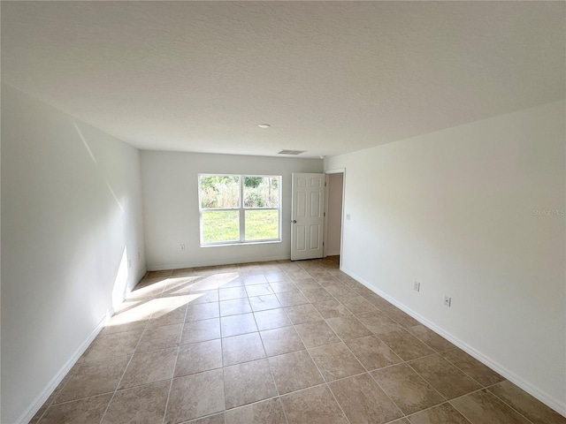 empty room with a textured ceiling and light tile patterned floors