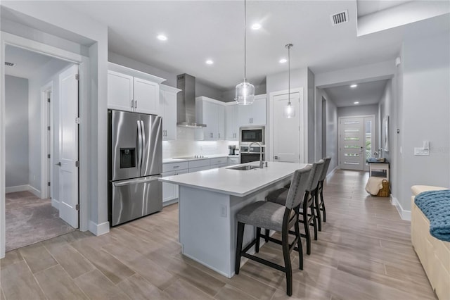 kitchen featuring stainless steel refrigerator with ice dispenser, white cabinetry, built in microwave, and wall chimney exhaust hood