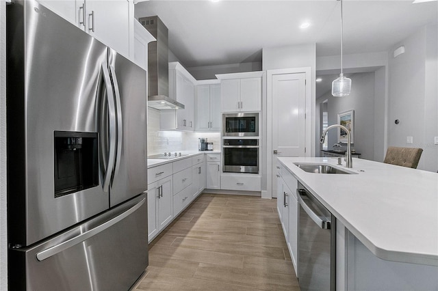 kitchen featuring appliances with stainless steel finishes, hanging light fixtures, wall chimney exhaust hood, sink, and white cabinetry