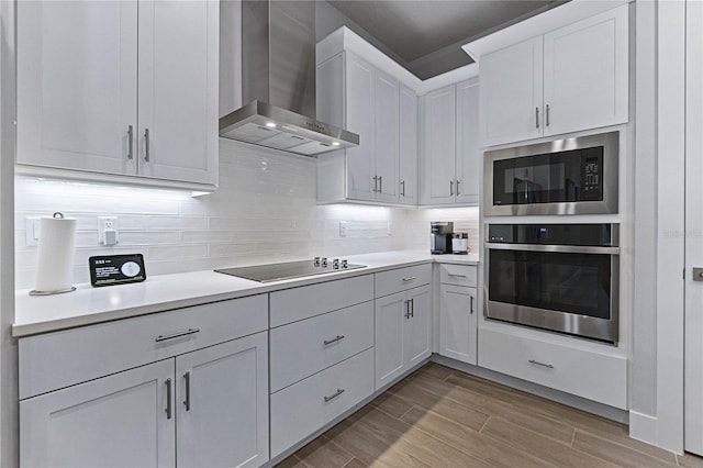 kitchen with stainless steel oven, wall chimney exhaust hood, built in microwave, black electric cooktop, and white cabinetry