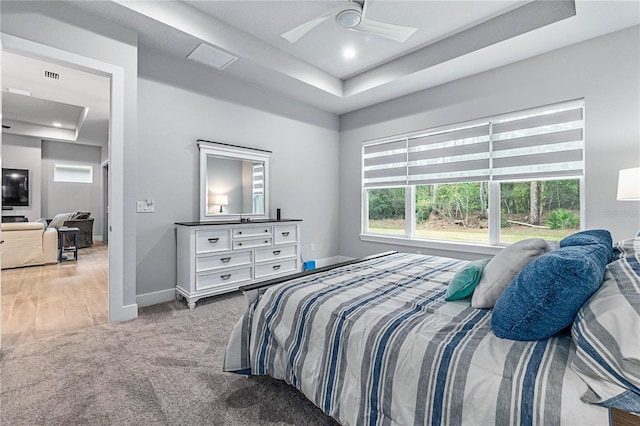 carpeted bedroom with ceiling fan and a tray ceiling