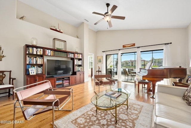 living room with ceiling fan, light hardwood / wood-style floors, and vaulted ceiling