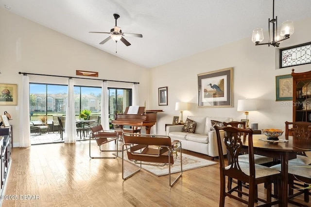 living room with ceiling fan with notable chandelier, high vaulted ceiling, and light hardwood / wood-style flooring