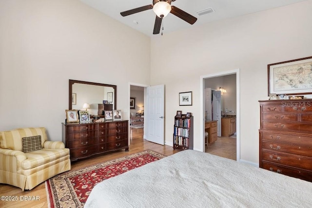 bedroom with ceiling fan, light hardwood / wood-style floors, a towering ceiling, and ensuite bath