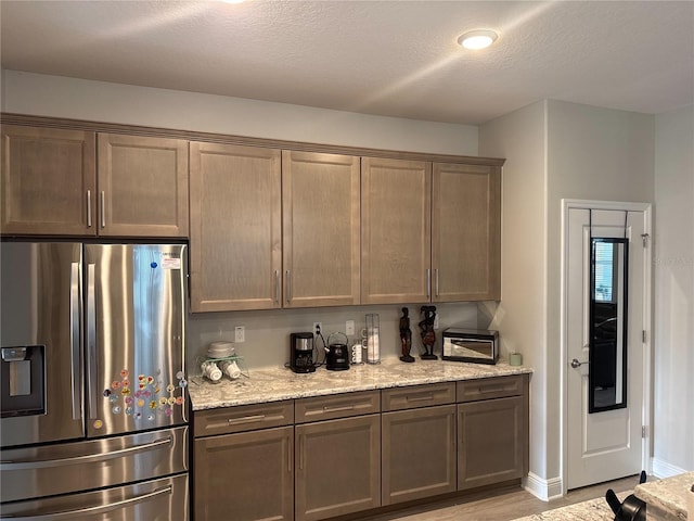 kitchen featuring light hardwood / wood-style floors, a textured ceiling, light stone counters, and stainless steel fridge with ice dispenser