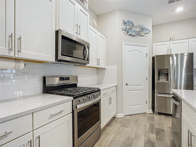 kitchen with light stone countertops, backsplash, appliances with stainless steel finishes, and white cabinetry