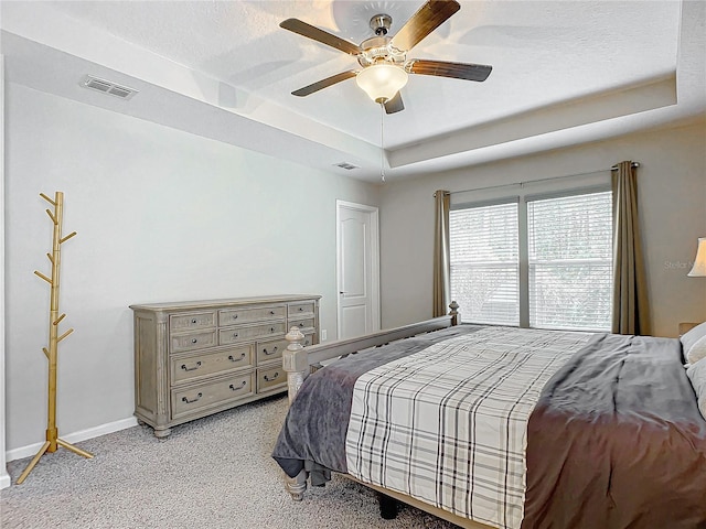 carpeted bedroom with ceiling fan and a raised ceiling