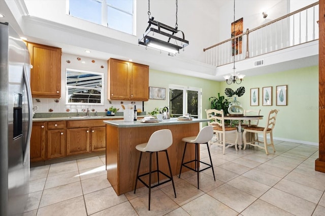 kitchen with stainless steel refrigerator with ice dispenser, decorative light fixtures, a center island, and a towering ceiling