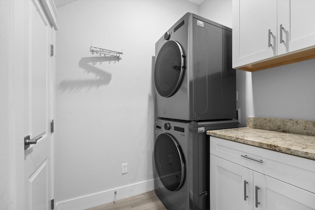 laundry area with stacked washer / dryer, cabinets, and light hardwood / wood-style floors