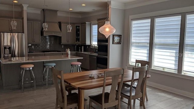 kitchen featuring custom range hood, backsplash, light stone countertops, pendant lighting, and appliances with stainless steel finishes