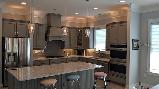 kitchen featuring a kitchen breakfast bar, custom exhaust hood, stainless steel appliances, pendant lighting, and sink