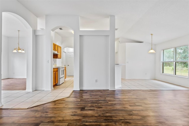 empty room with lofted ceiling, a notable chandelier, and light wood-type flooring