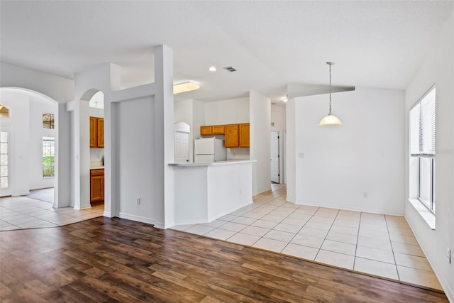 interior space with light hardwood / wood-style flooring, decorative light fixtures, vaulted ceiling, and white fridge