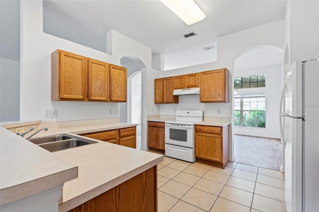 kitchen featuring sink, white appliances, light tile patterned floors, a textured ceiling, and kitchen peninsula