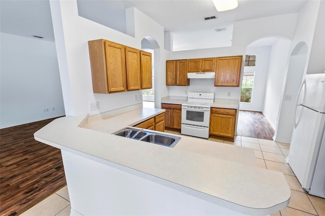 kitchen with sink, a kitchen breakfast bar, light tile patterned floors, kitchen peninsula, and white appliances