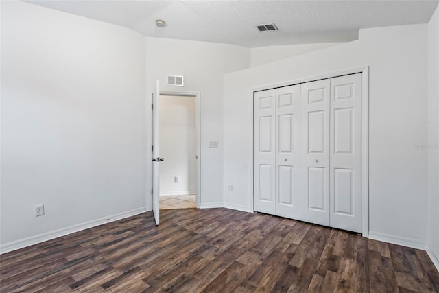 unfurnished bedroom with dark hardwood / wood-style flooring, vaulted ceiling, a closet, and a textured ceiling