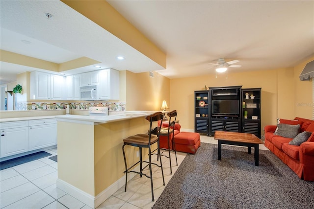 kitchen featuring light tile patterned floors, white cabinets, ceiling fan, and a breakfast bar