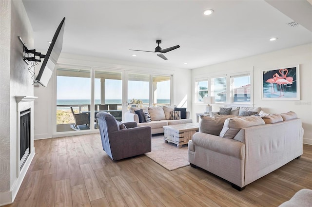 living room with ceiling fan, a water view, and light hardwood / wood-style floors